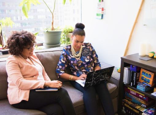 Duas mulheres conversando em uma sala confortável olhando para um notebook